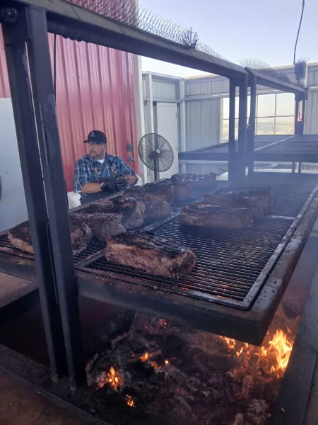 A cook turning cuts of tri-tip on the grate above the oak coals of the BBQ pit.