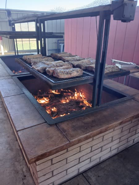 Tri-tip cooking over an open oak fire on the adjustable grate of the ranch's Santa Maria–style BBQ pit.